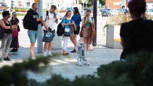 Na zdjęciu grupa przechodniów robiąca zdjęcia platformy kroczącej (pies robot)