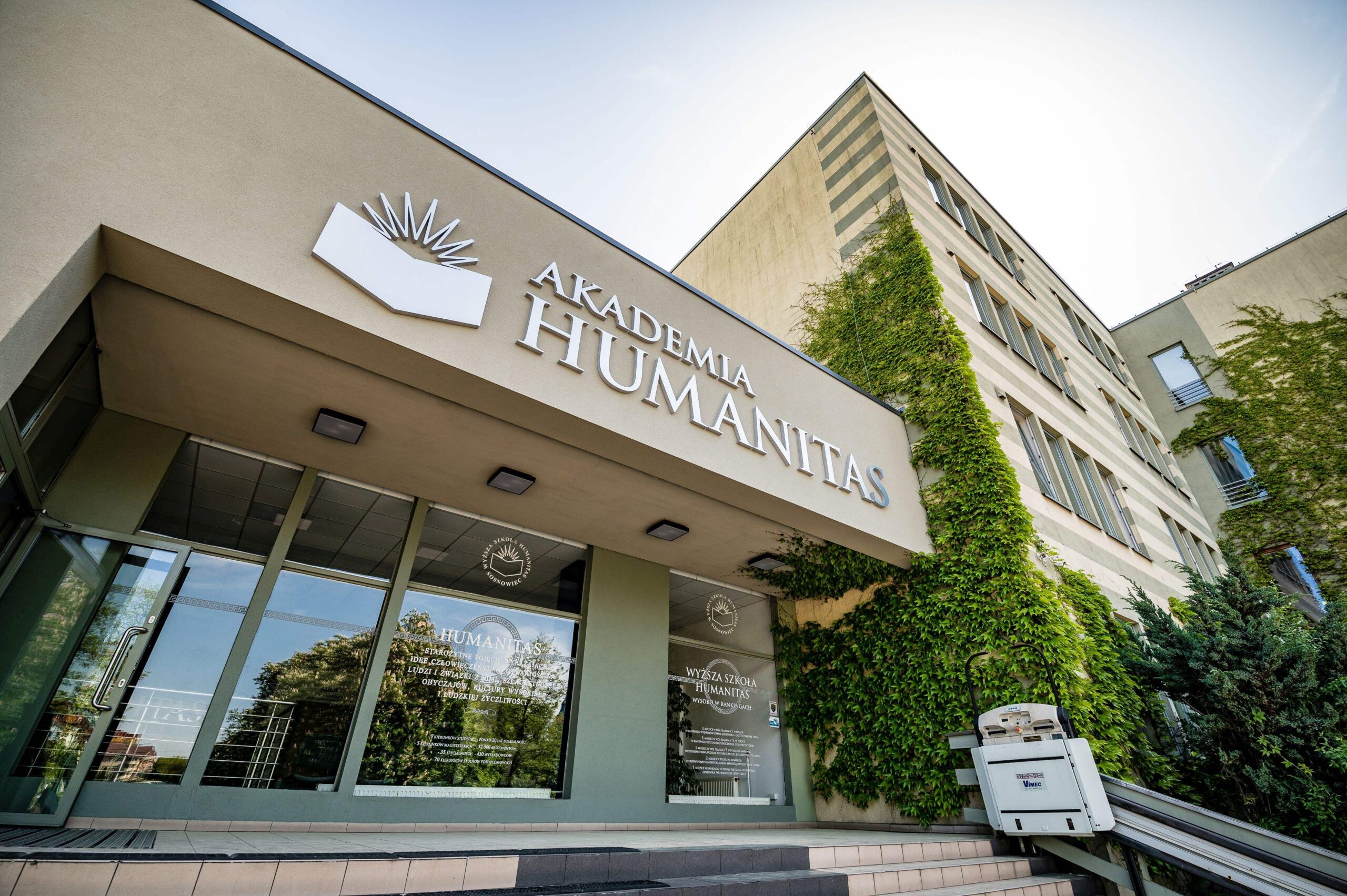 Wejście główne do budynku Akademii Humanitas w Sosnowcu otoczone zielenią w słoneczny dzień.