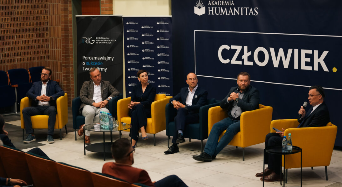 Panel dyskusyjny z udziałem sześciu prelegentów siedzących w fotelach na scenie, prowadzony w Akademii Humanitas. W tle baner z logo Akademii Humanitas i Regionalnej Izby Gospodarczej w Katowicach. Na stolikach stoją butelki z wodą, mikrofony i notatki.