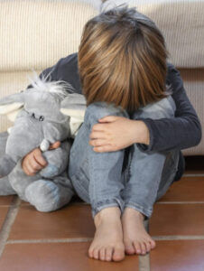 Smutne dziecko siedzące na podłodze z pluszową zabawką w ręku.