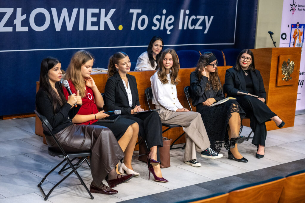 Uczestniczki debaty podczas Girls Week w Akademii Humanitas. Kobiety siedzą na krzesłach. W tle granatowe tło z logotypem uczelni.