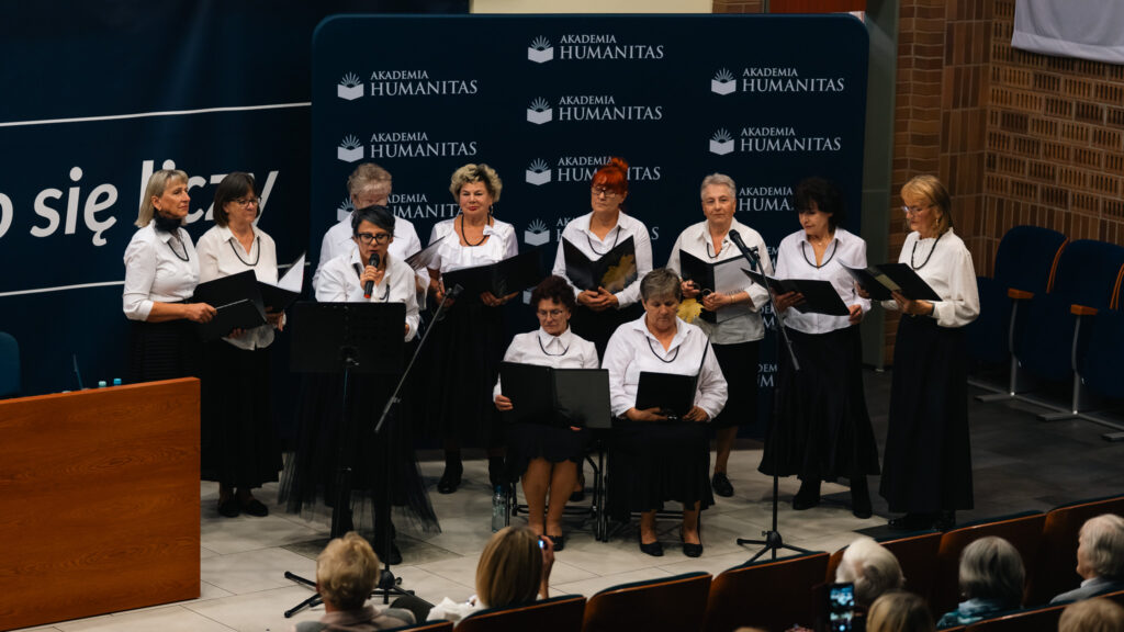 Zespół kobiet śpiewający podczas wydarzenia w Akademii Humanitas, stojący na scenie przed publicznością.