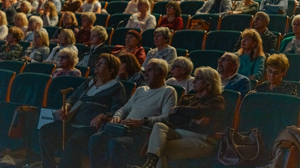 Seniorzy siedzący na auli w Akademii Humanitas, oglądający występ podczas wydarzenia.