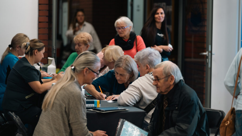 Seniorzy korzystają z badań profilaktycznych przy stolikach w Akademii Humanitas.