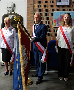 Poczet sztandarowy z trzema osobami stoi podczas Inauguracji Uniwersytetu Trzeciego Wieku, trzymając sztandar z orłem w koronie.