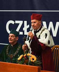 Zdjęcie przedstawia Inaugurację Roku Akademickiego. Na pierwszym planie przemawia Rektor Akademii Humanitas, dr Mariusz Lekston. Na drugim planie, za stołem prezydialnym, zasiada Aleksander Dudek, Kanclerz i założyciel Akademii Humanitas. Osoby na zdjęciu są ubrane w uroczyste togi akademickie.