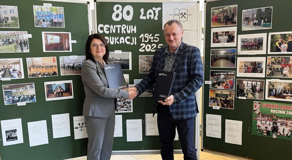 Kobieta i mężczyzna podają sobie ręce podczas podpisania współpracy z Akademią Humanitas, na tle tablicy z napisem „80 lat Centrum Edukacji 1945–2025”