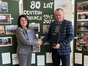 Kobieta i mężczyzna podają sobie ręce podczas podpisania współpracy z Akademią Humanitas, na tle tablicy z napisem „80 lat Centrum Edukacji 1945–2025”