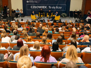 Debata w Akademii Humanitas – pełna aula i prelegenci rozmawiający na scenie przed publicznością.