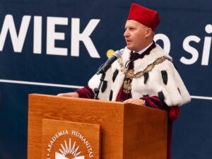 Rektor dr Mariusz Lekston w todze i birecie Akademii Humanitas przemawia z mównicy podczas uroczystości akademickiej.