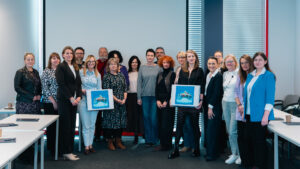 Grupa kilkunastu dorosłych osób stojących w sali konferencyjnej na tle dużego ekranu. Uczestnicy ustawieni w kilku rzędach, uśmiechnięci, w półformalnych strojach. Są to uczestnicy Brunchu oświatowego Akademii Humanitas.