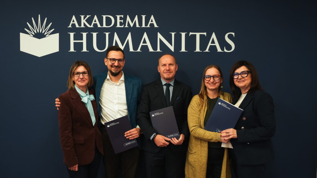 Grupa pięciu osób stojących przed logo Akademii Humanitas z teczkami uczelni po podpisaniu porozumienia.