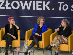 Trzy kobiety prowadzące rozmowę podczas panelu dyskusyjnego w Akademii Humanitas, w tle baner z napisem „Człowiek. To się liczy”.