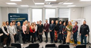 Grupa kilkunastu osób stoi w dwóch rzędach w sali konferencyjnej, pozując do wspólnego zdjęcia. W tle znajdują się roll-upy Akademii Humanitas i Szkoły Psychoterapii