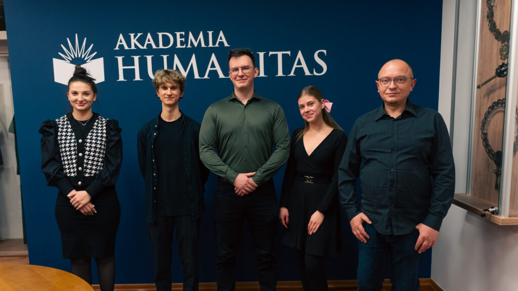 Grupowe zdjęcie pięciu osób stojących przed ścianką z logo Akademii Humanitas, wykonane w przestrzeni uczelni. Uczestnicy pozują do pamiątkowej fotografii po spotkaniu akademickim.