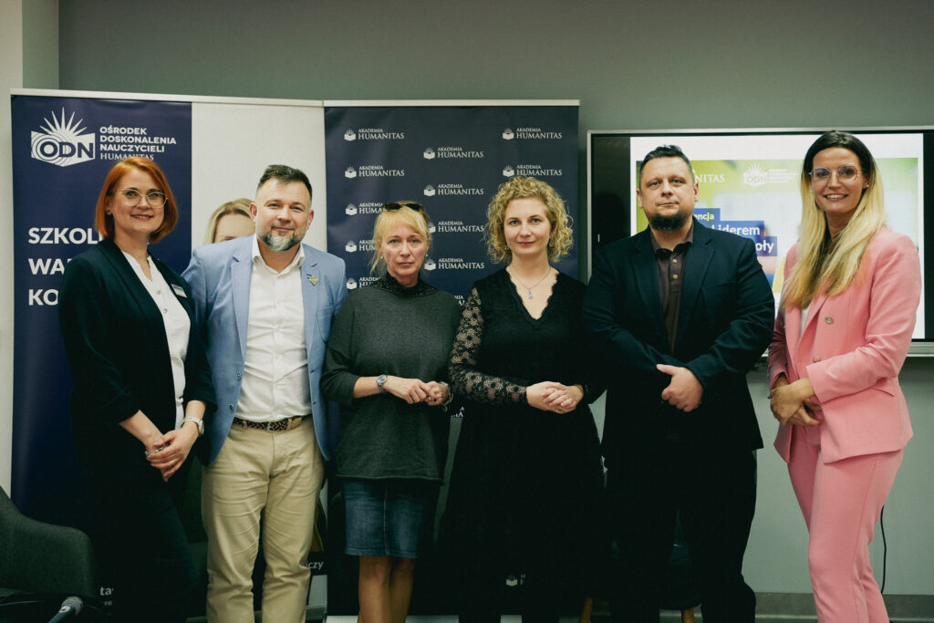 Wspólne zdjęcie sześciu uczestników wydarzenia edukacyjnego w Akademii Humanitas – kobiety i mężczyźni stoją obok siebie przed roll-upami uczelni i ODN, w sali konferencyjnej.