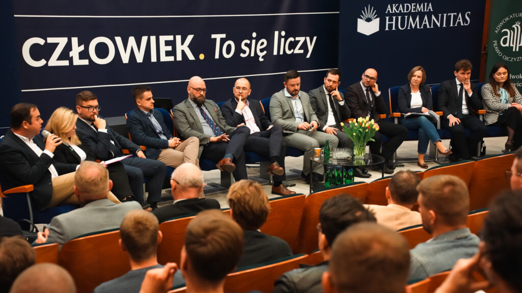 Panel dyskusyjny w Akademii Humanitas – prelegenci siedzą na scenie przed banerem z hasłem »Człowiek. To się liczy«, prowadzą rozmowę z udziałem publiczności zgromadzonej w auli.