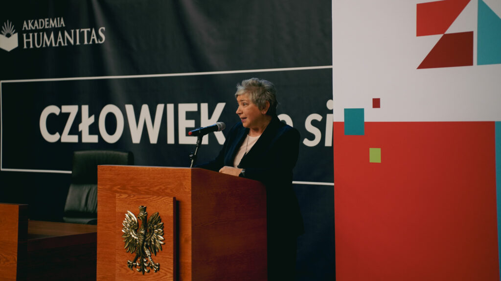 Kobieta przemawia przy mównicy z mikrofonem podczas wydarzenia w Akademii Humanitas; w tle baner z hasłem „Człowiek. To się liczy” oraz elementy graficzne Zagłębiowskiego Maratonu Nauki.