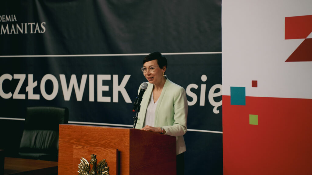 Kobieta przemawia przy mównicy z mikrofonem podczas wydarzenia w Akademii Humanitas; w tle baner z hasłem „Człowiek. To się liczy” oraz elementy graficzne Zagłębiowskiego Maratonu Nauki.