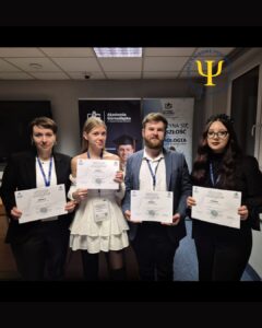 Cztery osoby stoją obok siebie w pomieszczeniu konferencyjnym, każda trzyma w dłoniach dyplom za zajęcie I miejsca; w tle widoczne są roll-upy promocyjne oraz logo Koła Naukowego Psychologii Akademii Humanitas.