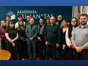 Grupowe zdjęcie zespołu Akademii Humanitas stojącego przed ścianką z logo uczelni. Uczestnicy pozują do wspólnej fotografii w eleganckim, oficjalnym otoczeniu.