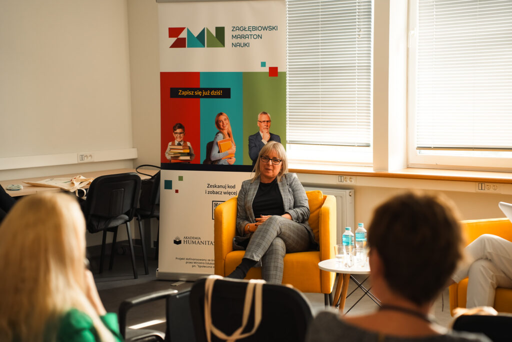 Uczestniczka siedzi w żółtym fotelu i rozmawia z publicznością; w tle roll-up „Zagłębiowski Maraton Nauki”.