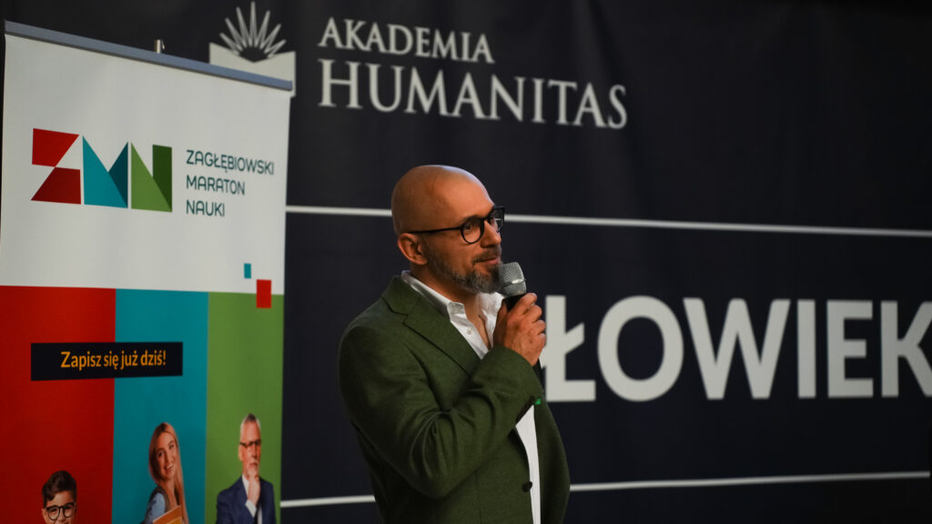 Prelegent z mikrofonem przemawia na scenie; w tle baner Akademii Humanitas i „Zagłębiowski Maraton Nauki”.