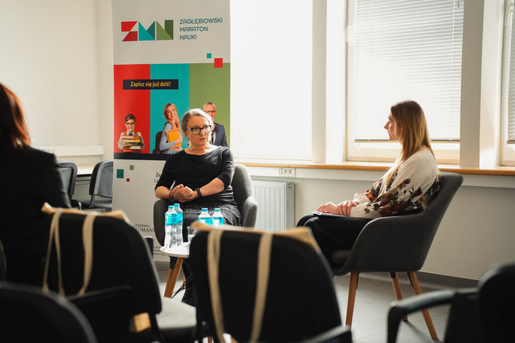 Dwie uczestniczki siedzą w fotelach i prowadzą rozmowę podczas spotkania; w tle roll-up „Zagłębiowski Maraton Nauki”.