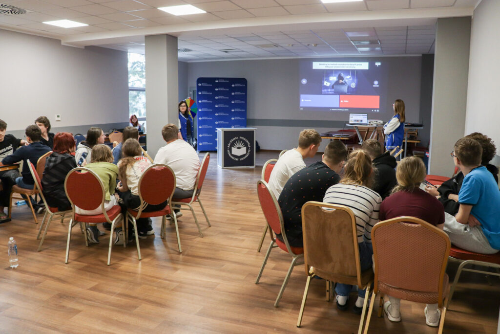Uczniowie siedzą przy stolikach w sali Akademii Humanitas i biorą udział w interaktywnym quizie wyświetlanym na ekranie.