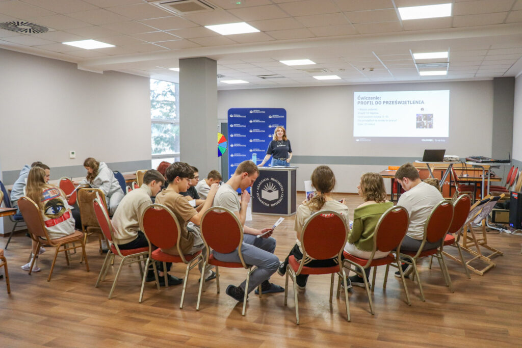 Uczniowie siedzą w kręgu i wykonują zadanie podczas warsztatów.