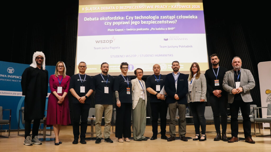 Na zdjęciu widać grupę uczestników II Śląskiej Debaty o Bezpieczeństwie Pracy w Katowicach w 2026 roku stojących na scenie do wspólnego zdjęcia.

Za nimi znajduje się duży ekran z tytułem wydarzenia oraz tematem debaty oksfordzkiej o wpływie technologii na bezpieczeństwo pracy. Uczestnicy mają identyfikatory konferencyjne i stoją w jednym rzędzie na tle sceny.