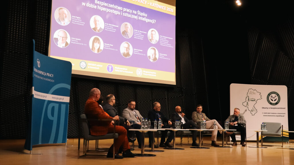 Na zdjęciu widać panel dyskusyjny podczas debaty o bezpieczeństwie pracy. Kilku ekspertów siedzi na scenie w fotelach i rozmawia, a jeden z nich trzyma mikrofon.

Nad nimi wyświetlony jest slajd z tytułem panelu oraz zdjęciami i nazwiskami prelegentów. Po bokach sceny znajdują się plansze z logotypami instytucji związanych z bezpieczeństwem pracy.