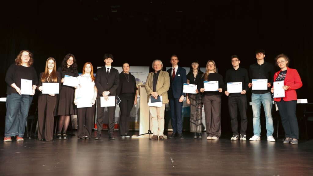 Grupa uczestników stoi na scenie z certyfikatami po zakończeniu debaty.