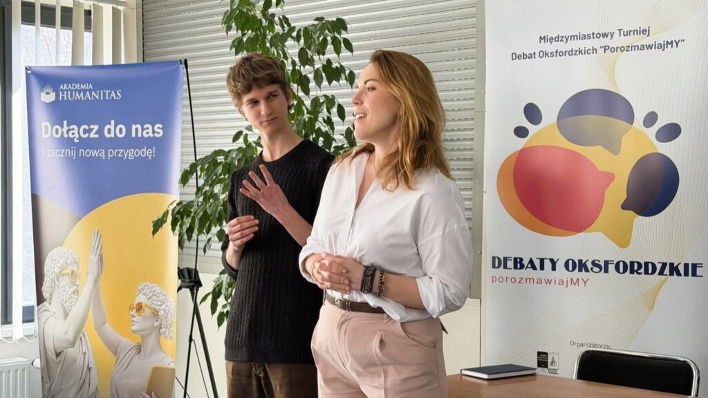 Dwie osoby prowadzą wystąpienie w sali. W tle banery Akademii Humanitas i turnieju debat oksfordzkich.