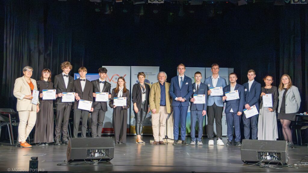 Grupa uczestników stoi na scenie z certyfikatami po zakończeniu debaty.