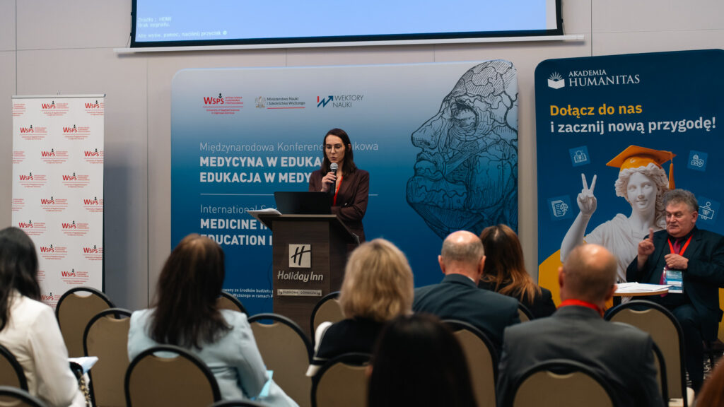 Prelegentka występuje przy mównicy podczas międzynarodowej konferencji naukowej „Medycyna w edukacji. Edukacja w medycynie”. W sali widoczni są uczestnicy, banery konferencyjne oraz baner Akademii Humanitas z hasłem „Dołącz do nas i zacznij nową przygodę!”.