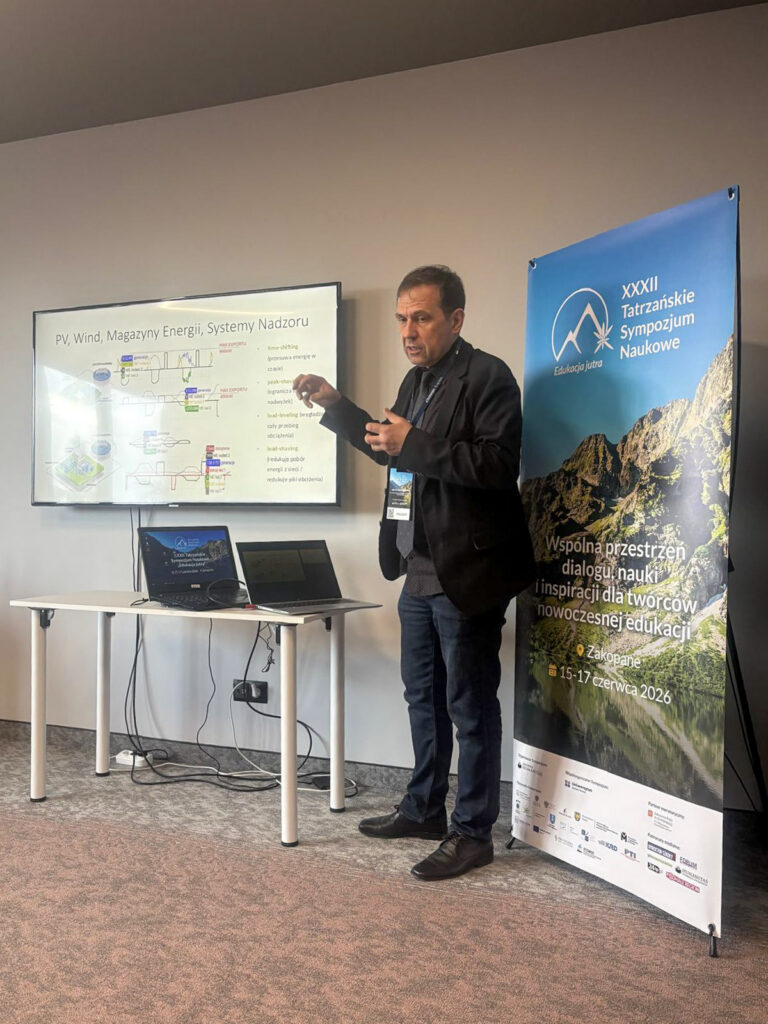 Prelegent podczas XXXIII Tatrzańskiego Sympozjum Naukowego omawia prezentację dotyczącą energii odnawialnej, magazynów energii i systemów nadzoru. Obok ekranu z diagramami stoi baner wydarzenia „Edukacja Jutra” w Zakopanem.