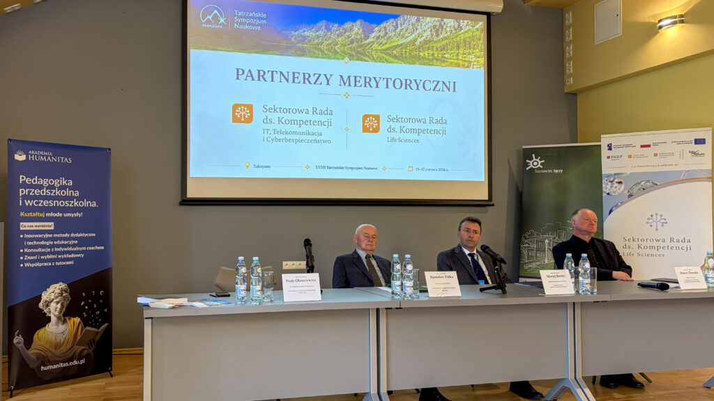 Panel dyskusyjny podczas XXXIII Tatrzańskiego Sympozjum Naukowego w Zakopanem. Przy stole siedzą prelegenci, a na ekranie widoczny jest slajd z partnerami merytorycznymi: Sektorową Radą ds. Kompetencji IT, Telekomunikacja i Cyberbezpieczeństwo oraz Sektorową Radą ds. Kompetencji Life Sciences.