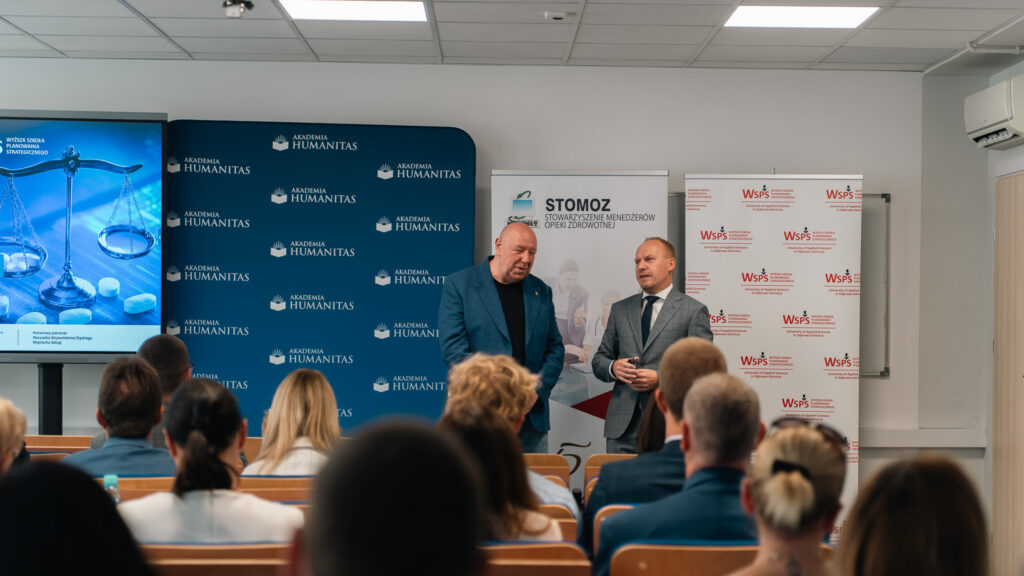 Dwóch mężczyzn stoi na tle ścianki Akademii Humanitas oraz roll-upów STOMOZ i WSPS. Przemawiają w stronę publiczności.