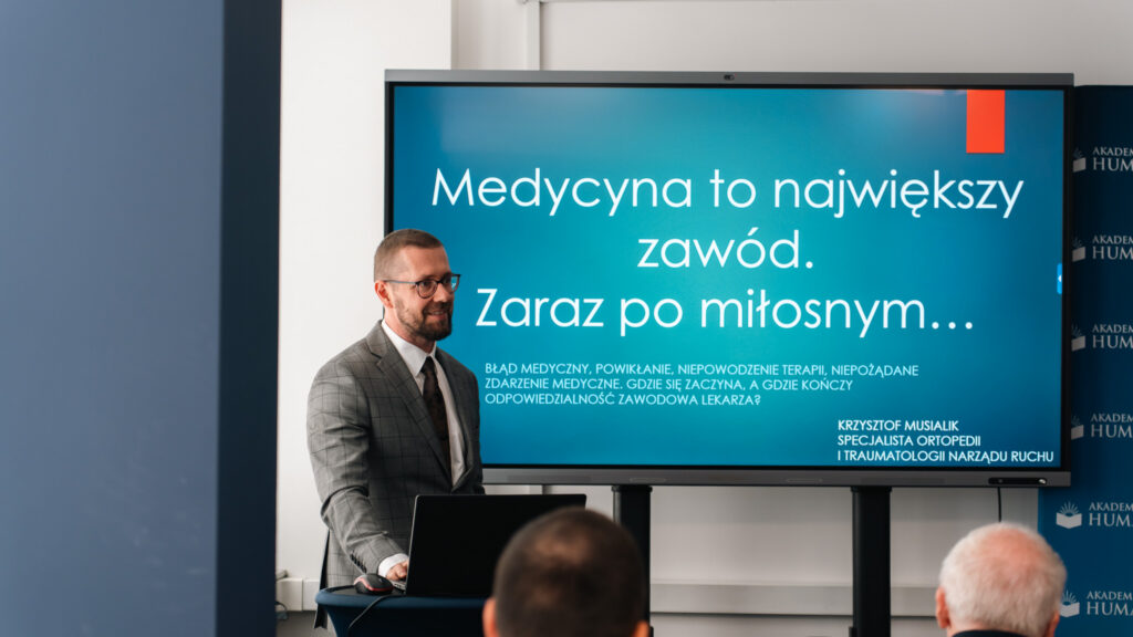 Prelegent stoi przy telewizorze ze slajdem "Medycyna to największy zawód, zaraz po miłosnym....",