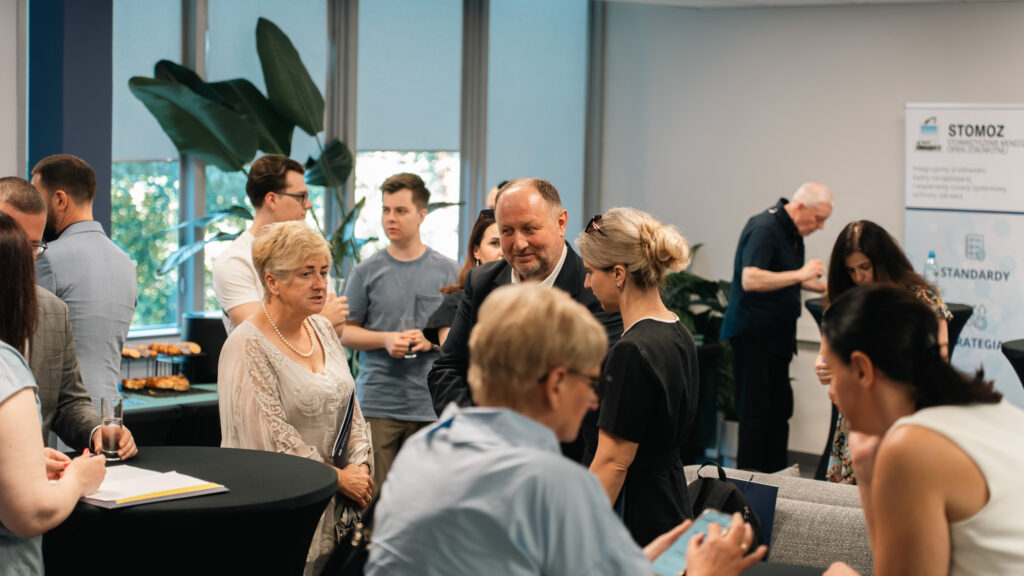 Uczestnicy konferencji stoją przy stolikach kawowych podczas przerwy.