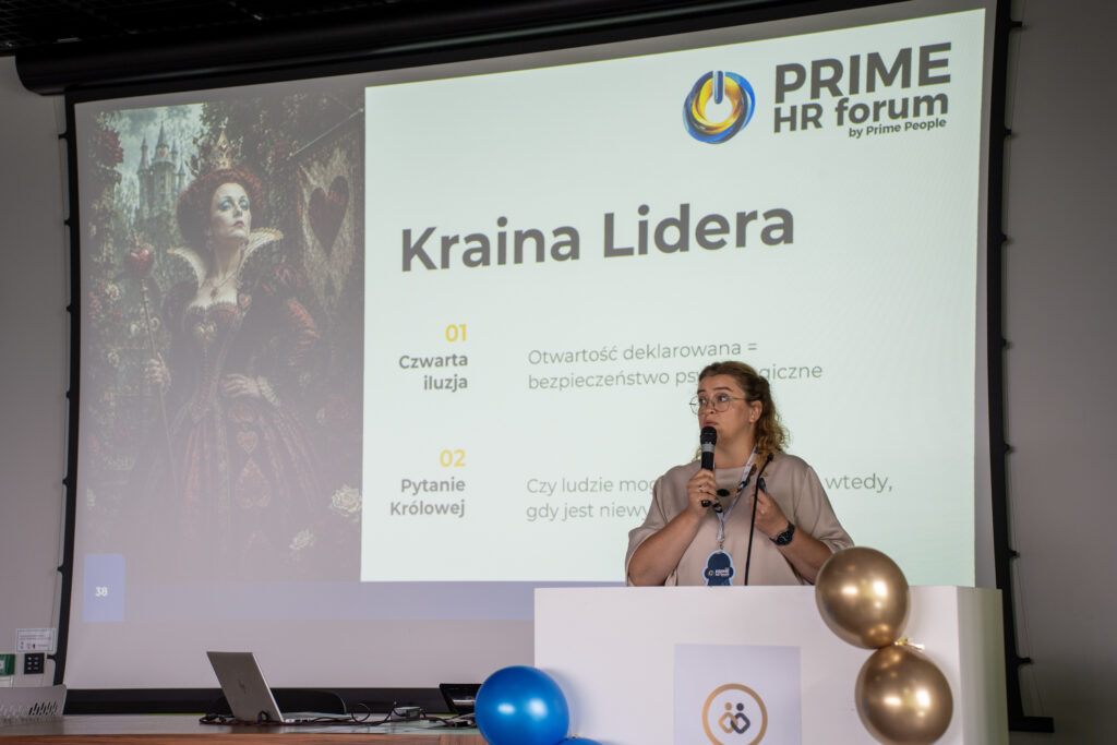 Prelegentka występuje przy mównicy podczas Prime HR Forum, trzymając mikrofon. Na ekranie za nią widoczny jest slajd „Kraina Lidera” z ilustracją królowej oraz punktami dotyczącymi otwartości i bezpieczeństwa psychologicznego.