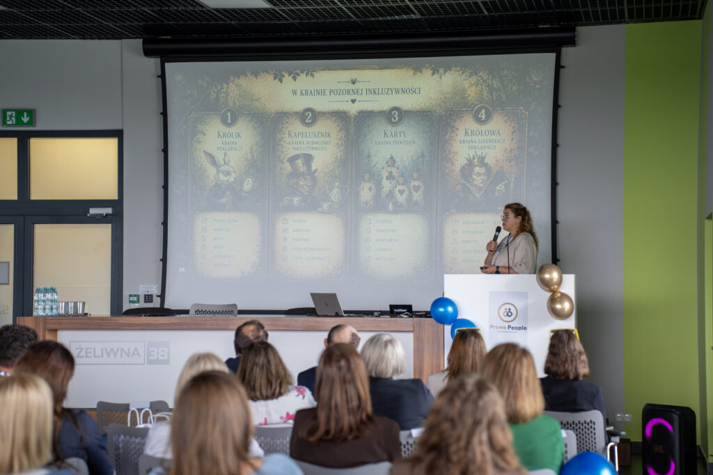 Prelegentka występuje przy mównicy podczas Prime HR Forum, prezentując temat pozornej inkluzywności. Na dużym ekranie widoczny jest slajd inspirowany motywami z „Alicji w Krainie Czarów”, a publiczność siedzi w sali konferencyjnej i słucha wystąpienia.