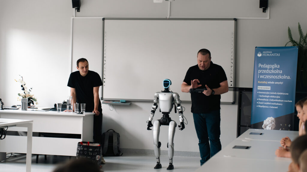 Prowadzący prezentuje humanoidalnego robota. Robot stoi przed uczestnikami, a w tle widoczny jest baner kierunku „Pedagogika przedszkolna i wczesnoszkolna”.