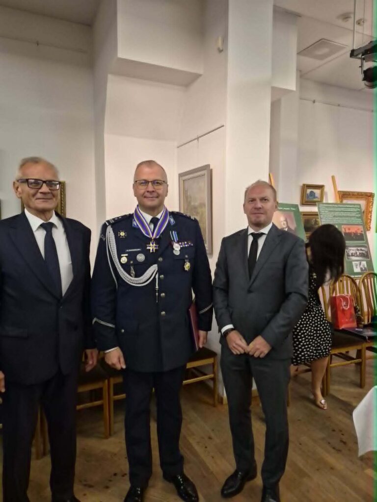 Trzech uczestników uroczystości, w tym Rektor Akademii Humanitas i umundurowany funkcjonariusz z odznaczeniami, pozujących do zdjęcia.