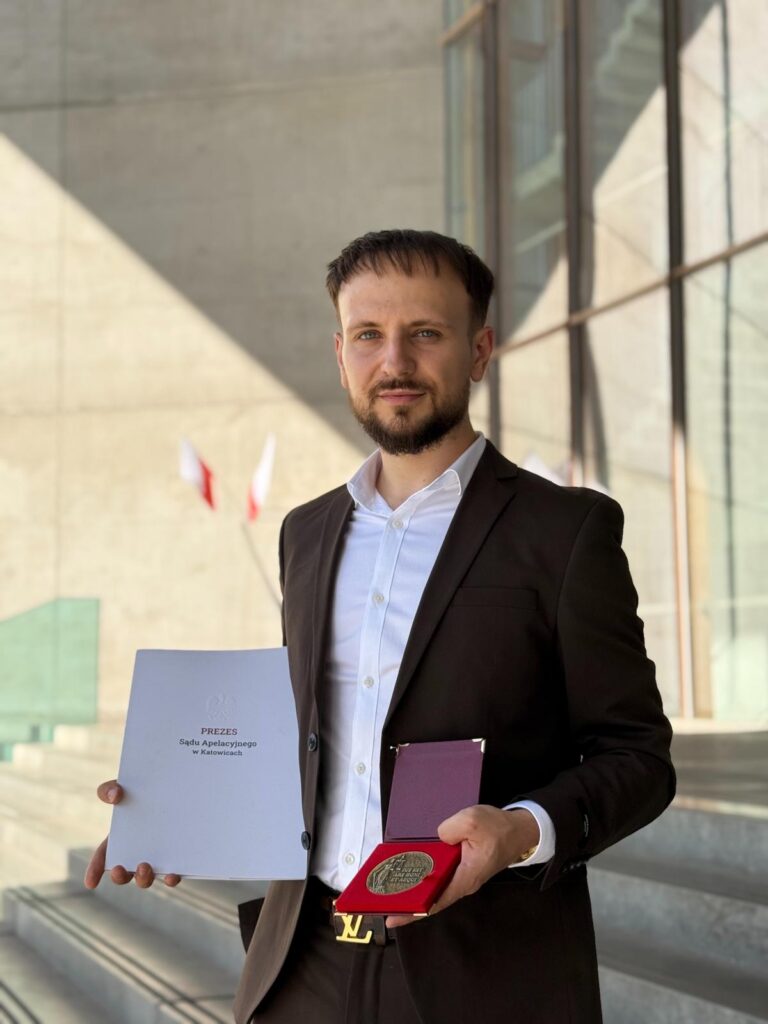 Student prawa Akademii Humanitas pozuje z medalem i teczką z napisem "Prezes Sądu Apelacyjnego w Katowicach". 