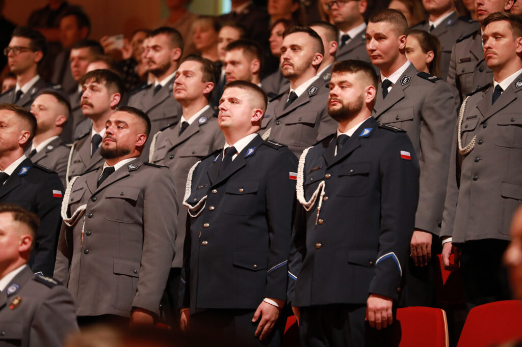 Grupa umundurowanych funkcjonariuszy stojąca w rzędach podczas uroczystości w sali.