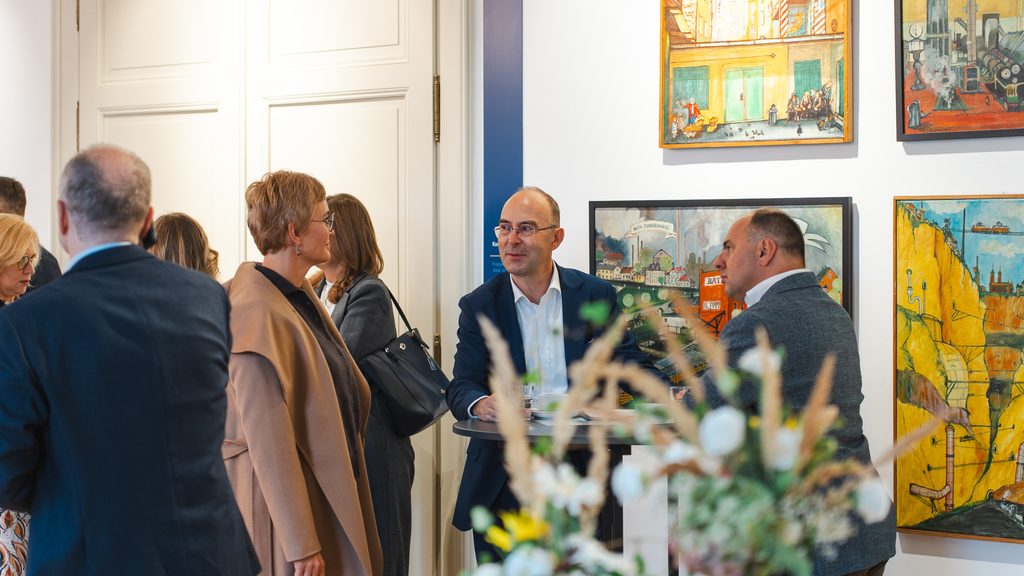 Uczestnicy spotkania networkingowego prowadzą rozmowy przy stoliku w przestrzeni wystawienniczej. W tle widoczne są obrazy oraz elementy dekoracyjne wnętrza.