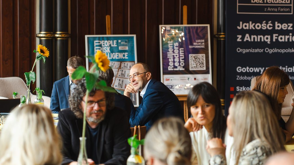 Uczestnicy Resilient Leaders Forum rozmawiają przy stolikach podczas przerwy networkingowej. W tle widoczne są plakaty wydarzenia oraz dekoracje ze słonecznikami.