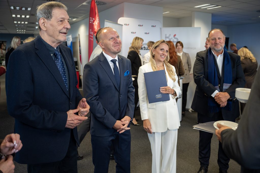 Uczestnicy wydarzenia rozmawiają podczas części networkingowej. W tle widoczne są ścianki KSeF oraz przestrzeń konferencyjna z gośćmi spotkania.